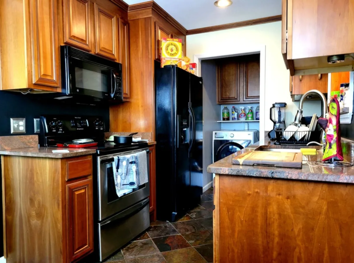 This image showcases a warmly lit kitchen featuring modern appliances, a spacious countertop, and inviting cabinetry. The sink and workspace are clean and welcoming, with space for multiple people to participate in meal preparation or conversation.