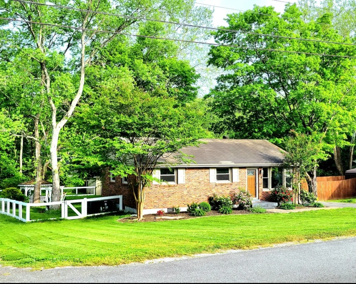 The brick exterior of a home set against a lush green lawn, framed by mature trees and flower beds. The porch area is ideal for enjoying quiet moments together, such as morning coffee or relaxing after an outing.