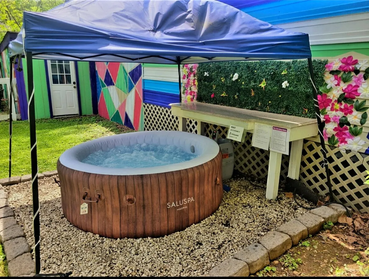 A stylish hot tub sits beside colorful wall art and a decorative fence, providing a tranquil spot for soaking and socializing. The setup exudes comfort and a touch of luxury within a private garden setting.