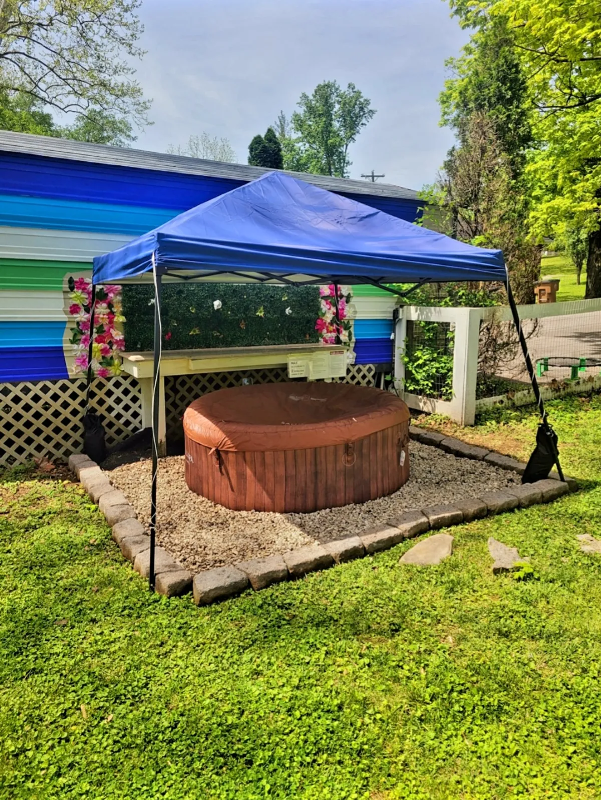 This image showcases an inviting hot tub set beneath a blue canopy in a lush backyard, surrounded by flower decorations and a green lawn. The setup hints at a private and festive space perfect for unwinding or celebrating with family after a day of adventure.