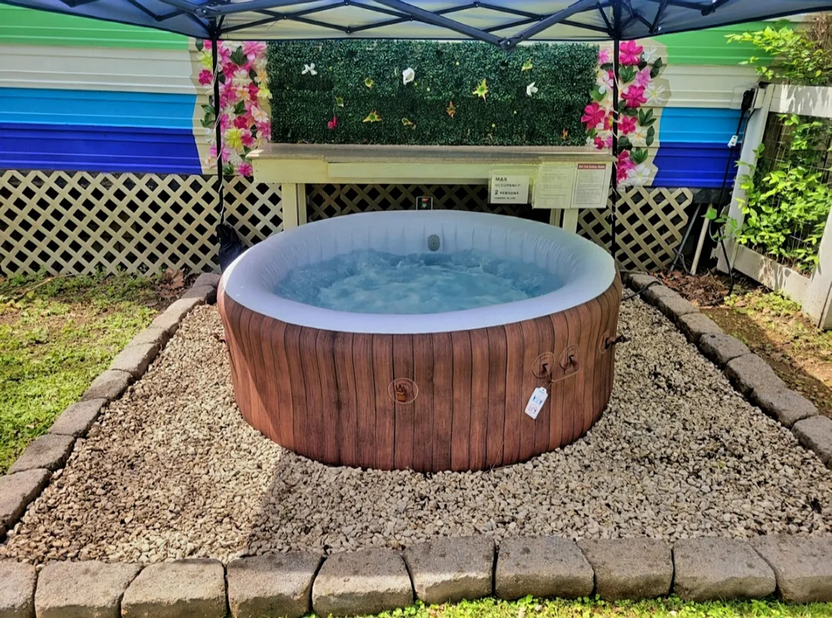 This image features a tranquil outdoor hot tub situated next to a decorative wall, surrounded by lush garden greenery. The inviting hot tub is the focal point, suggesting a perfect spot for group relaxation and socializing after a day of activities.