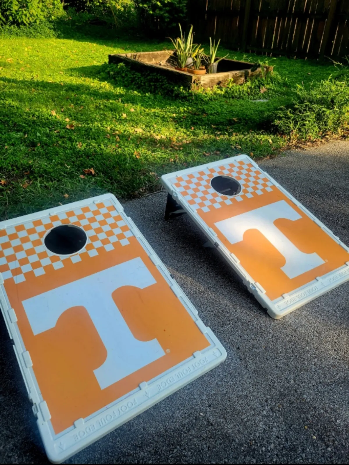 A set of cornhole boards is arranged on the green grass near a raised garden bed, ready for players to engage in a classic lawn game. The scene suggests a relaxed, playful environment ideal for all ages.